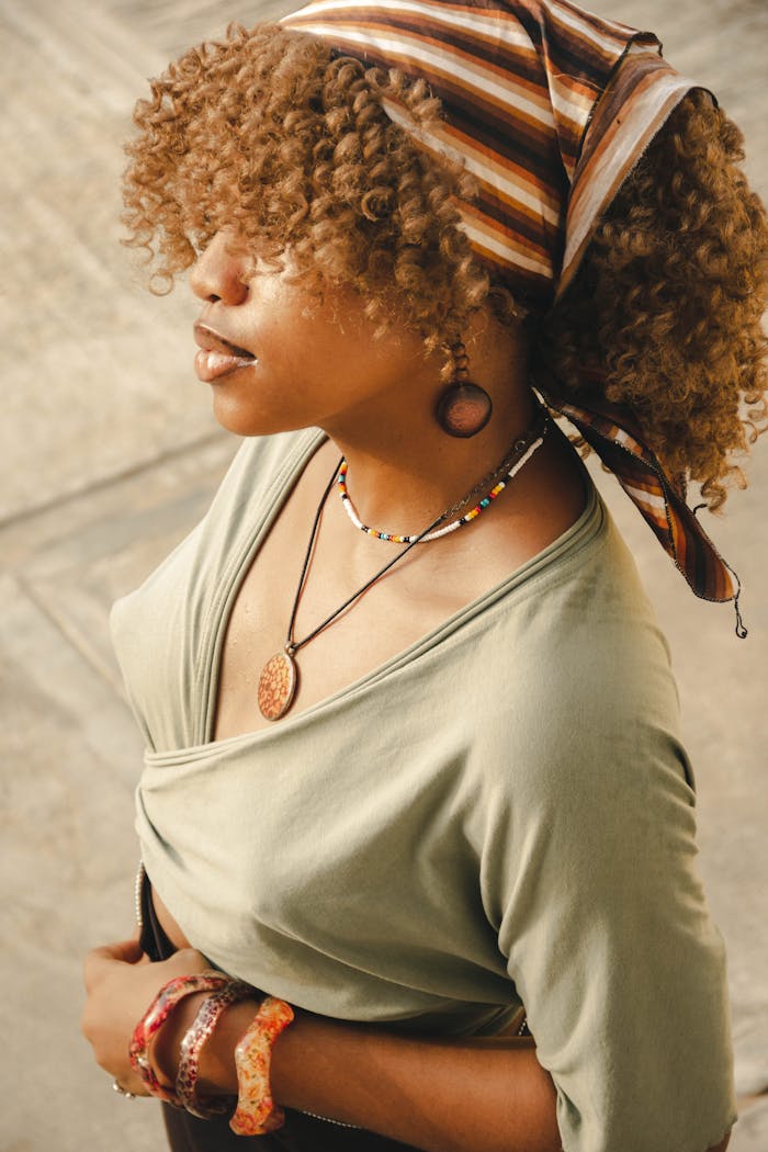 Portrait of a fashionable woman with curly hair and headscarf, wearing a necklace and bracelets.