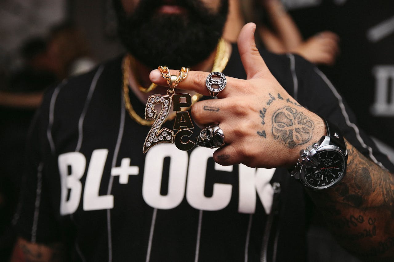 Close-up shot of jewelry, tattoos, and watch on a tattooed hand wearing a T-shirt.